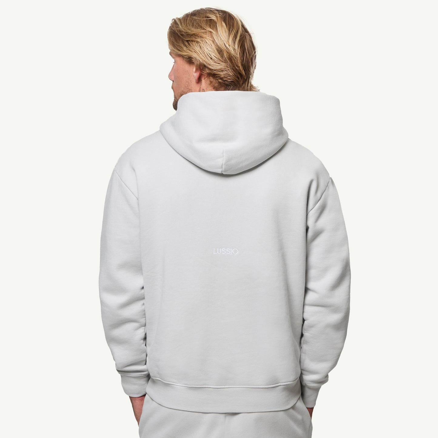 half body shot of back Lussio logo and hood shape and size, model looking away from the camera with hands in pockets, back view