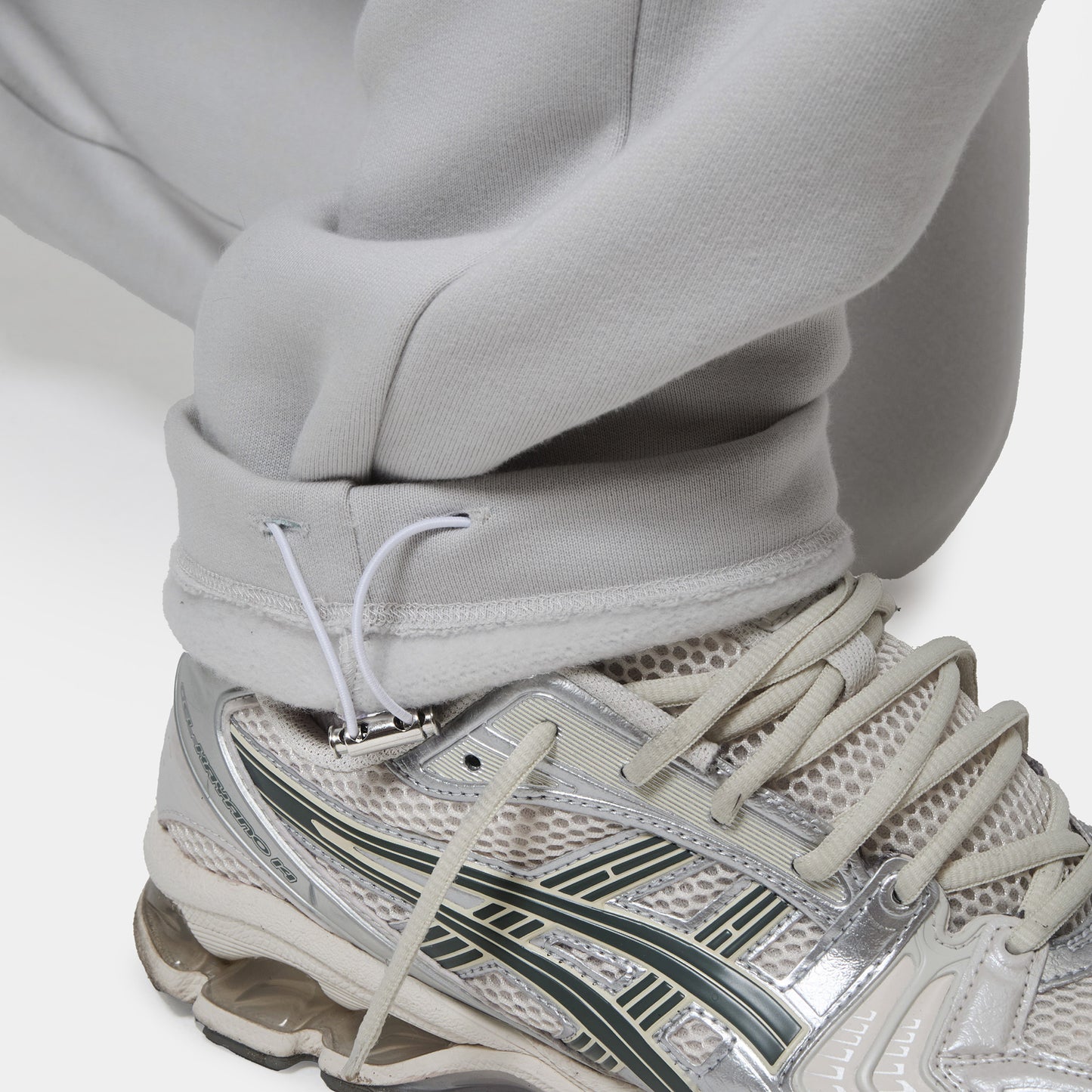 Close up shot of the the bottom drawcord, and the models trainers showing customers the details within the ice grey jogger, front view