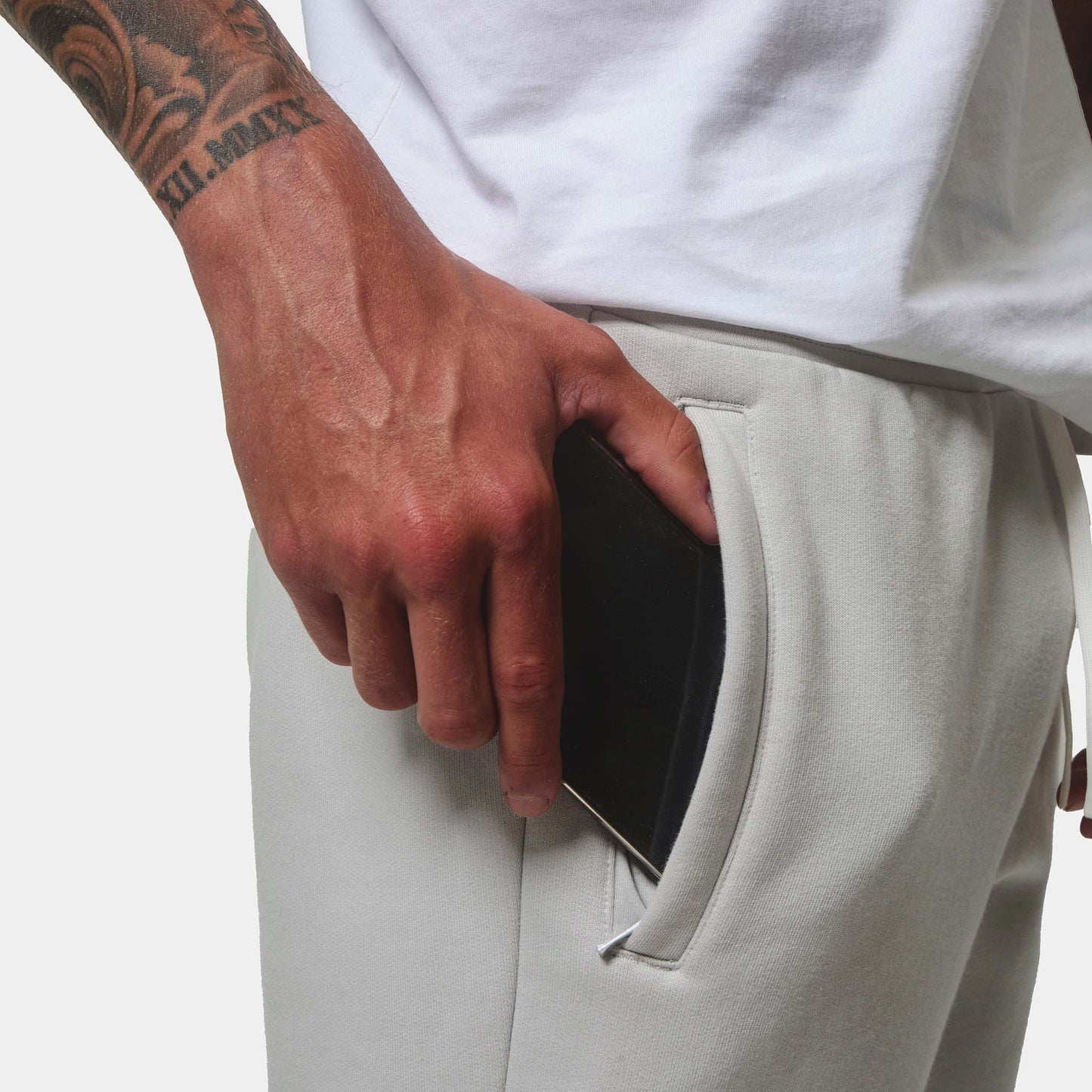 Close up on the ice grey jogger detail, model putting his phone into zip pocket, front view