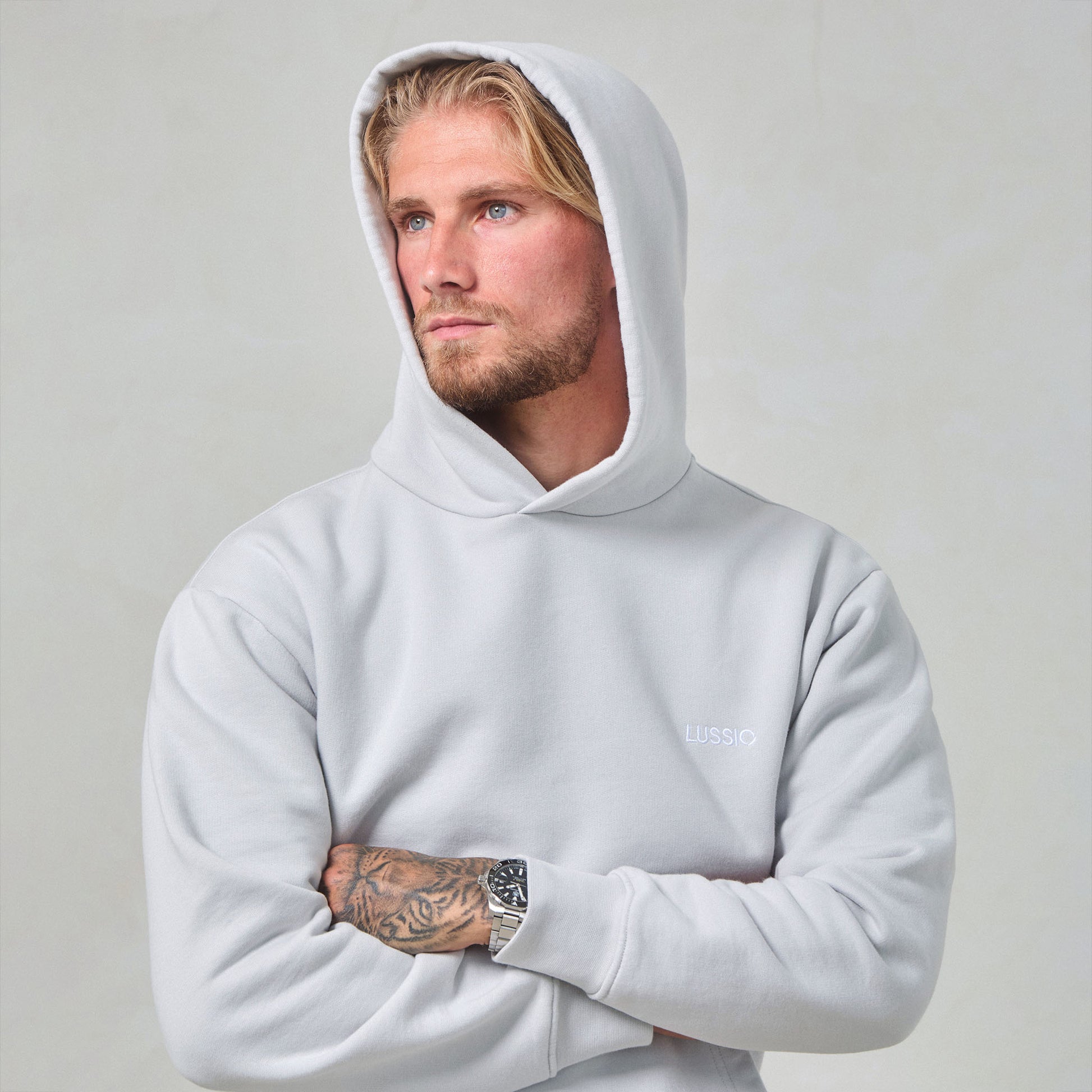 Model Posing with hood up looking away to the camera, crossing his arms wearing his Ice Grey Tracksuit, front view