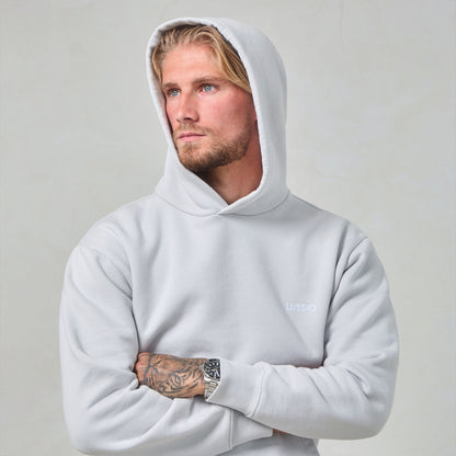 Model Posing with hood up looking away to the camera, crossing his arms wearing his Ice Grey Tracksuit, front view