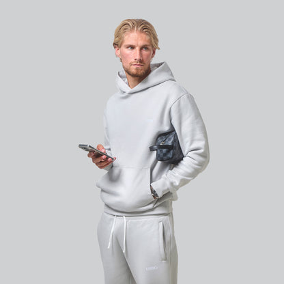 Model Posing looking away to the camera wearing his Ice Grey Tracksuit holding his phone and designer wash bag, front view