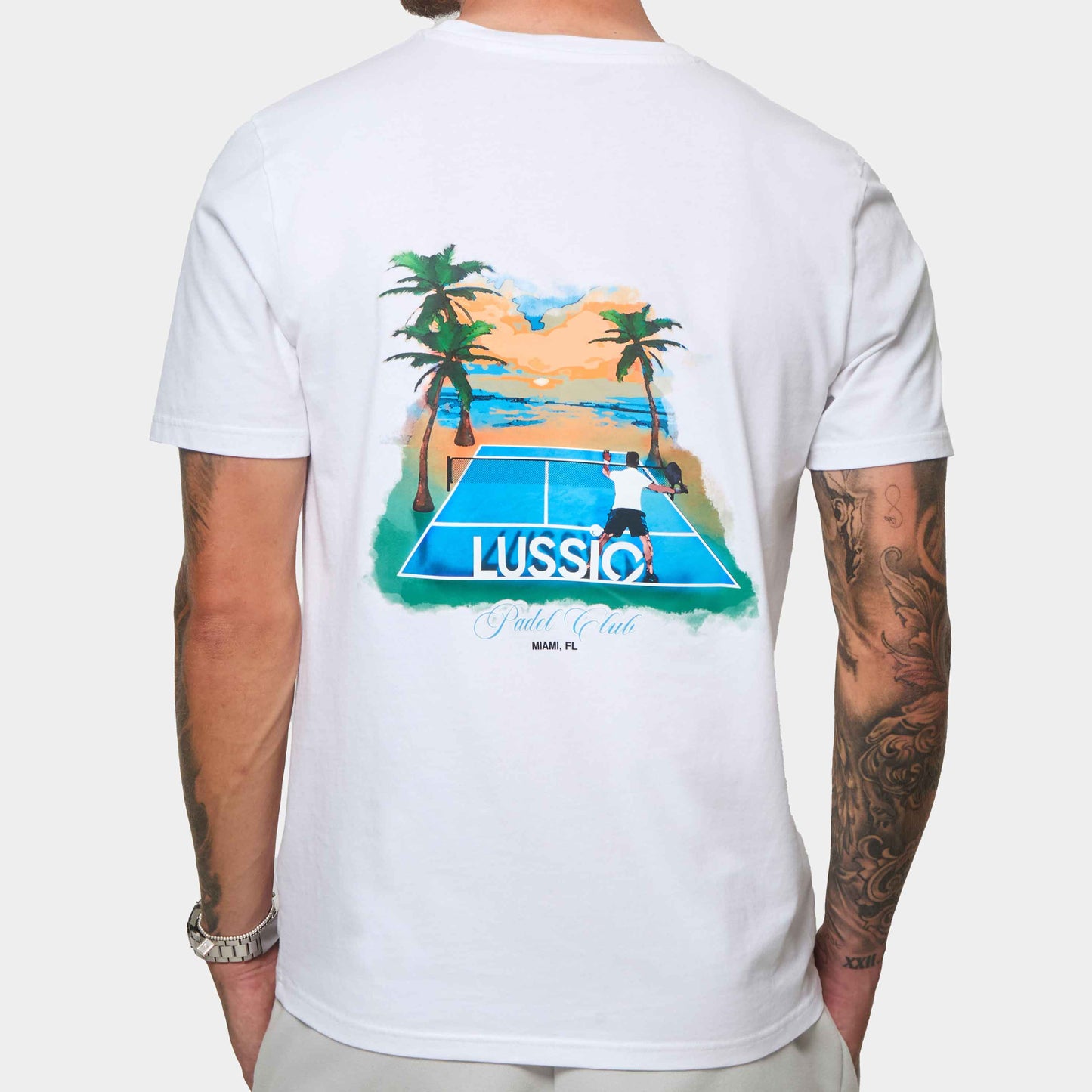 Model Posing away to the camera showing back print of his white/blue padel tee, back view