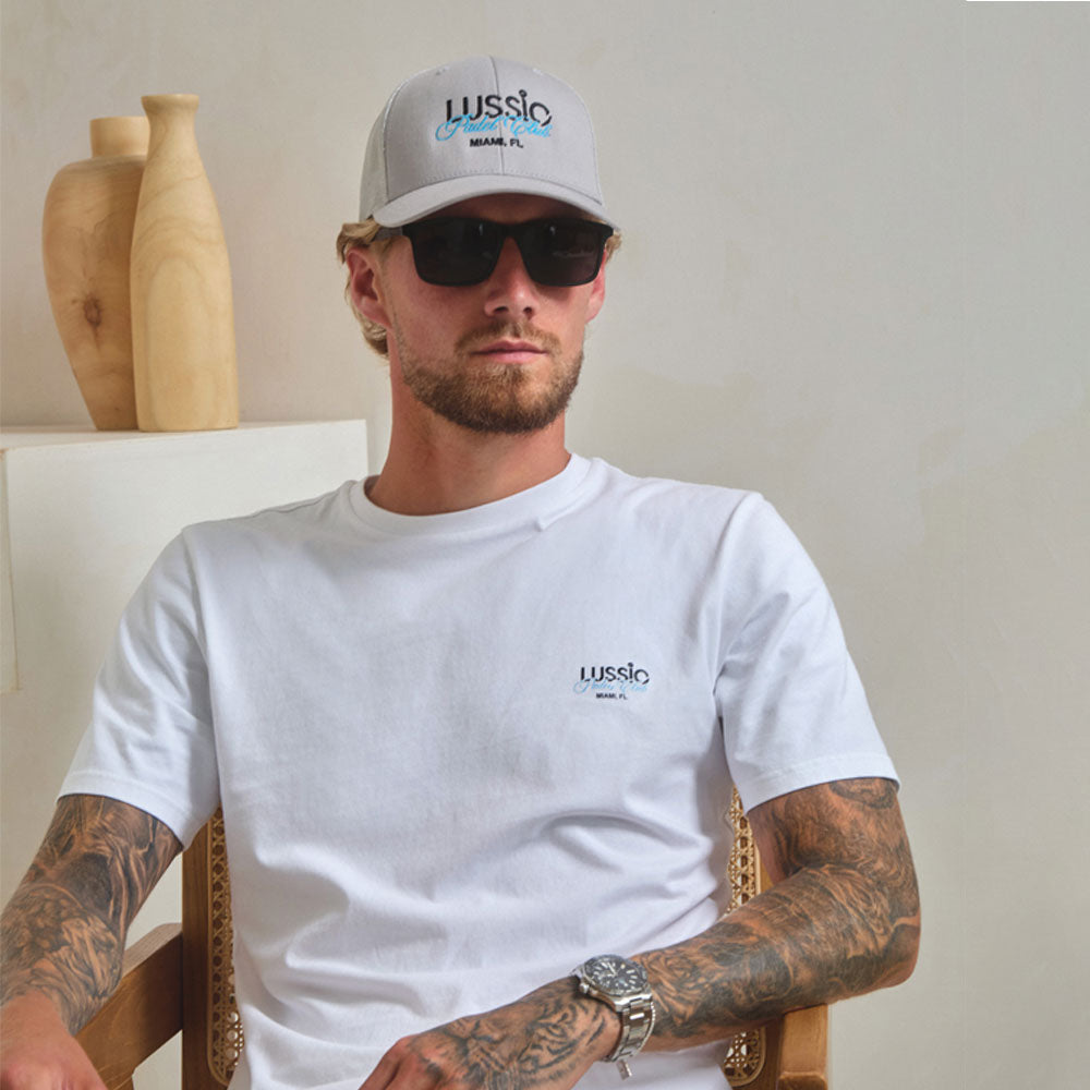 Model Posing to the camera wearing sunglasses, grey cap and his white/blue padel tee, front view